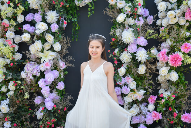 表情美丽的亚洲女人穿着白色的裙子站在黑色的花背景前美丽天肖像