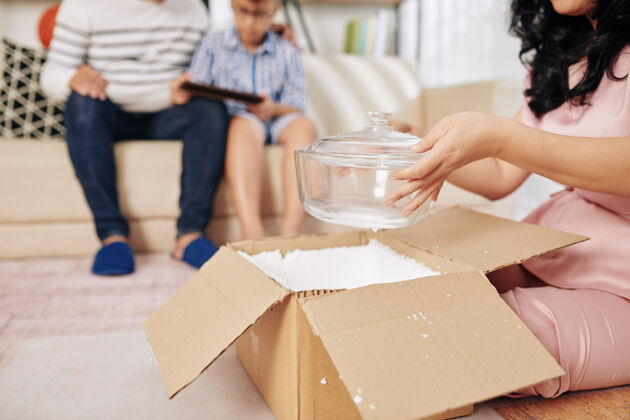 坐着一个女人坐在家里的地板上 从她收到的纸板箱里拿出新的玻璃碗休闲服搬家纸板箱