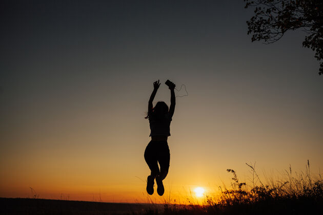 冒险兴奋的女孩在日落时跳跃享受轮廓夜晚