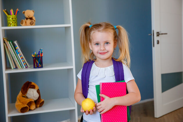 肖像一个手里拿着书和苹果的小女孩小学生背包童年