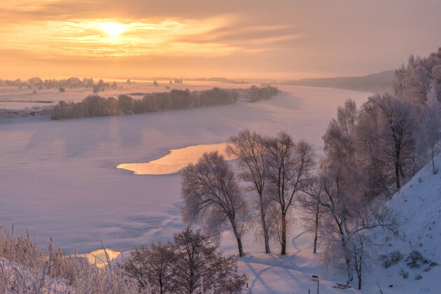 自然美丽的冬季景观日出在河上河岸上的树被雪覆盖了冰地平线河岸