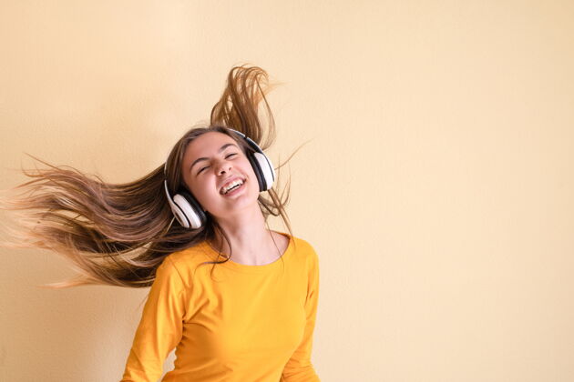 声音戴着耳机在黄色背景上跳舞的年轻女子欢乐表演人类