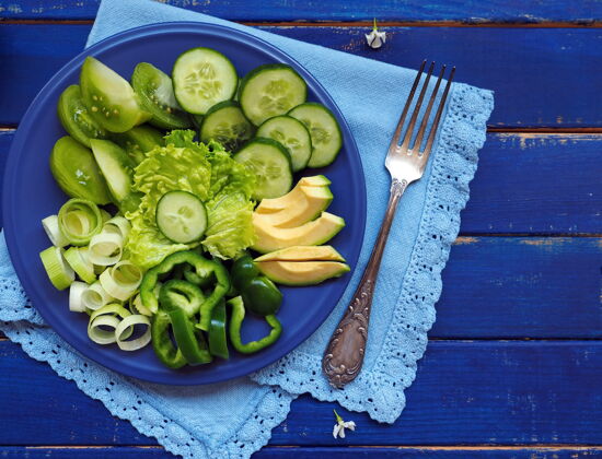 鳄梨绿色蔬菜和水果-沙拉生菜 黄瓜 韭菜 鳄梨 苹果和青椒在蓝色的木制表面苹果餐巾纸叶