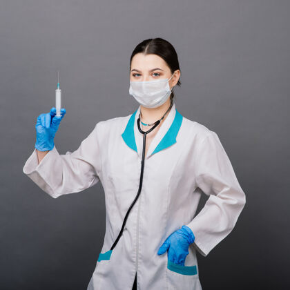 大流行严肃的女医生戴着医用口罩拿着注射器和疫苗隔离在灰色上严重听诊器分析