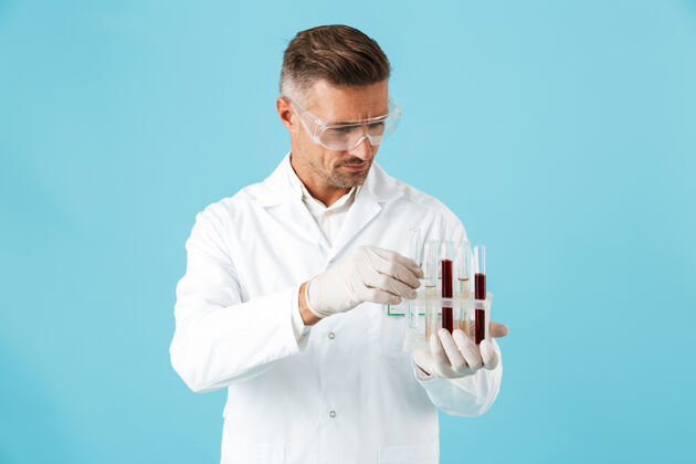 医学一位英俊严肃的成熟男子医生在蓝色的墙上举着带血的试管摆姿势医生服务药物