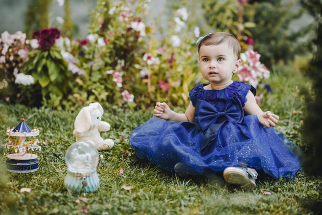户外公主惊奇地发现穿着蓝色裙子的小女孩坐在草地上 拿着她的玩具 看着某人高加索可爱坐着