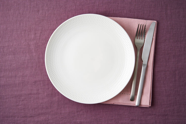 空白把空的白色盘子 叉子和刀子放在明亮的蓝莓红亚麻桌布上 放在桌子上 模型设置桌布复制空间