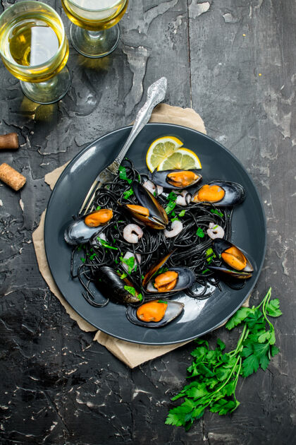 面条地中海食物意大利面用墨鱼墨 蛤蜊和白酒放在黑色的乡村餐桌上贝类海鲜顶部