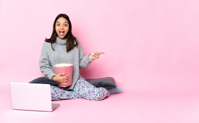 表演年轻女子一边吃爆米花一边在笔记本电脑上看电影 惊讶地指着一旁点人女人