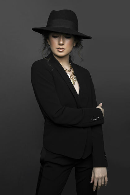 时尚前面的肖像是一位年轻漂亮的黑发女子 身穿黑色西装 戴着黑色帽子 带着化妆品 闭着眼睛 背景是灰色的年轻头发卷发