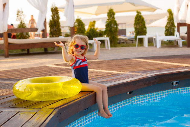 飞溅戴着墨镜和泳装的小女孩 夏天坐在游泳池边圆圈活动孩子