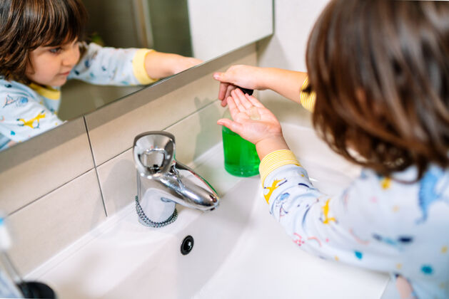 手穿着睡衣微笑的男孩照在镜子里 往手上倒肥皂洗手浴室健康无辜