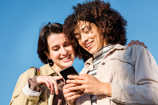 青少年两个年轻女子一边看着电话一边微笑聪明爱友谊