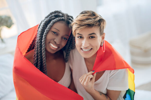 情侣快乐两个人带着彩虹旗的年轻女孩们 微笑着移情同性恋短发
