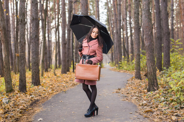 散步人 季节 时尚理念-美丽的年轻女子在秋园带伞吸引树叶黑发