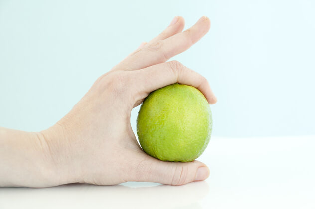 酸橙一个女人用食指和大拇指夹着一张白桌子上的酸橙新鲜生天然