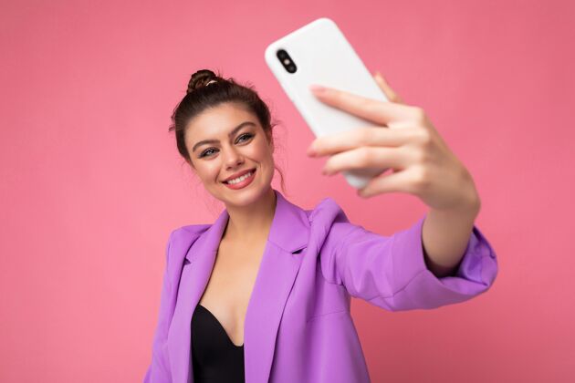 博客迷人迷人的年轻微笑的快乐女子手持和使用手机自拍穿着青年墙壁摄影师