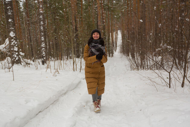 雪一个穿着棕色夹克的女孩在冬天的雪林里散步森林户外自然
