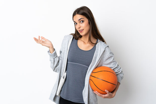 健身打篮球的年轻女子孤零零地站在白色的背景上 向侧面伸出双手 欢迎前来生活方式女性游戏