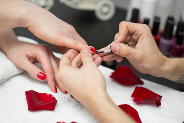 亚克力美甲特写美丽的女人在美容院用红色指甲油擦指甲拇指花瓣优雅