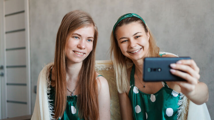 室内两位美丽快乐的女朋友在睡衣派对上用智能手机自拍数码设备快乐镜头