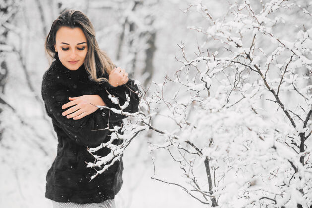 服装冬天 在雪林里 一个穿着毛皮大衣和连衣裙的漂亮女孩拥抱着自己 试图取暖公园年轻性感