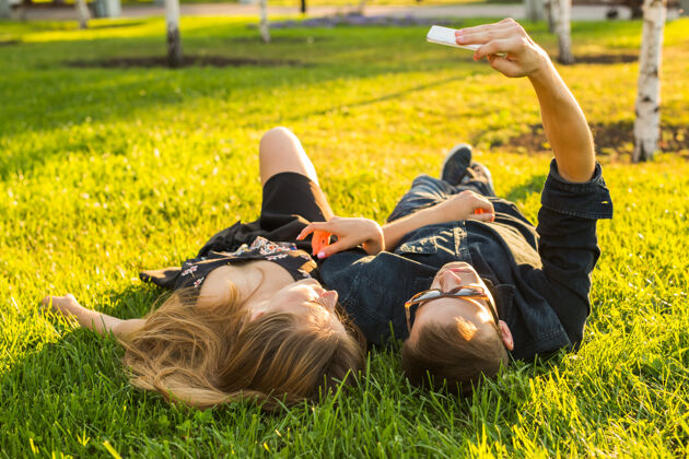 太阳镜爱与人概念快乐夏天 一对年轻夫妇躺在草地上 在智能手机上自拍男人肖像日期