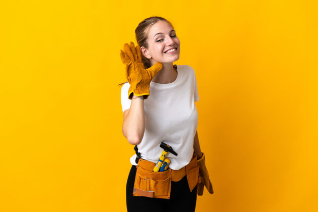 工艺一位年轻的电工女士被隔离在黄色背景下 用手捂着耳朵听东西年轻女孩木匠