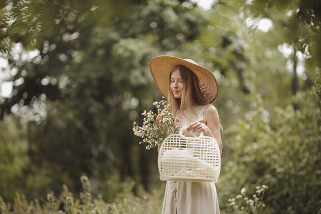 时尚一个时髦的女孩拿着一篮子田野穿过草地花年轻天生的金发女人户外散步服饰