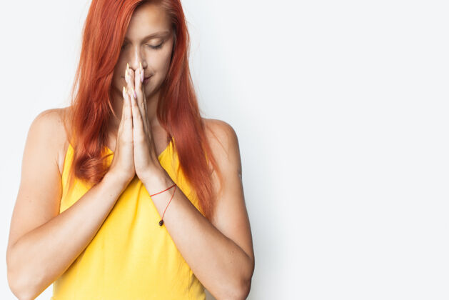 广告一位白人妇女双手合十 闭上眼睛 在白色的画室墙上祈祷空白和平放松