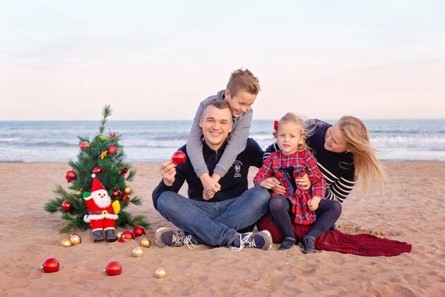 肖像一家人在海边过圣诞节树快乐父母带着儿子和小女儿海洋庆祝圣诞节