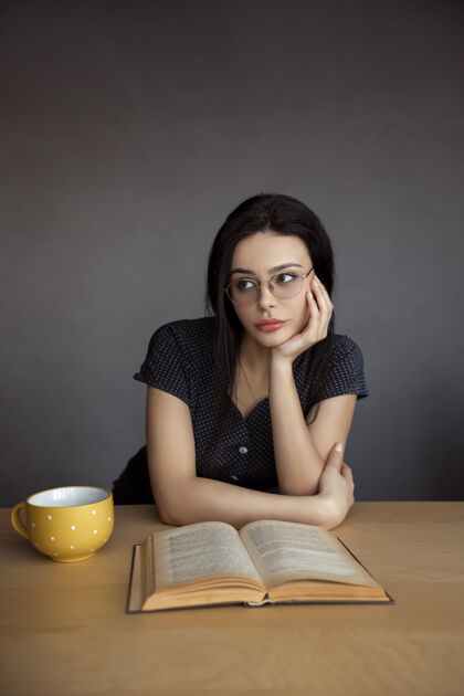 学校戴眼镜的漂亮年轻女子正在读一本书书无聊坐着喝茶学习的女孩大学成人室内