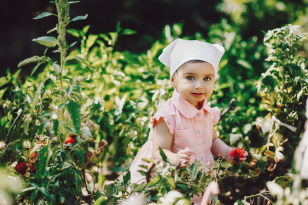 收获有趣的 可爱的婴儿用白色的头巾在花园里吃西红柿 对着镜头微笑快乐婴儿玩耍
