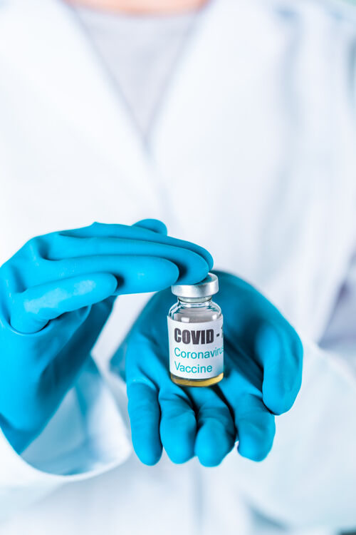 防护女医生或护士穿着制服 戴着手套 戴着口罩 在实验室里拿着带有冠状病毒疫苗标签的药瓶疫苗瓶医疗设备针头