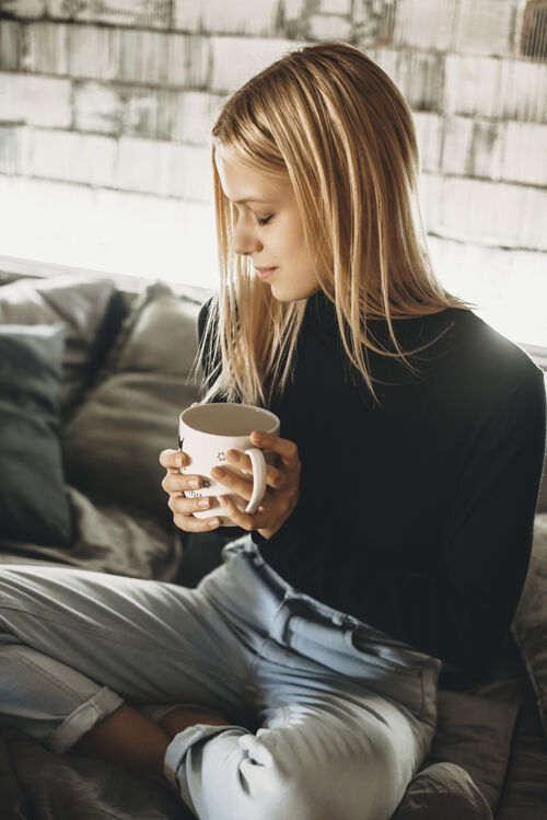 休闲舒适的年轻女性坐在家里的床上喝热咖啡女人浪漫杯子