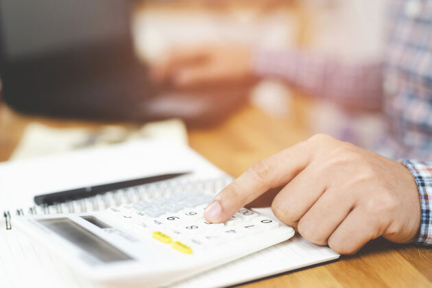 键盘特写：年轻人的手在笔记本上写字 在家里的办公室做财务工作时 他正在用计算器数笔记储蓄理财概念计划数据记事本