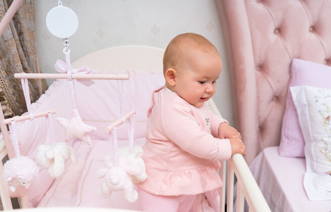 孩子一个快乐的婴儿在一个粉红色的婴儿床和卧室的场景与悬挂的手机关注警觉悬挂