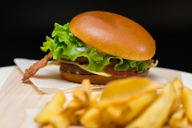 酒吧培根芝士汉堡放在一个硬皮的新鲜面包卷上 在木板上炸薯条 重点放在汉堡上手指食品薯条自助餐厅