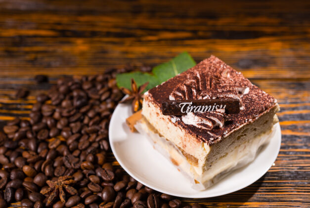 提拉米苏美味的方形蛋糕片放在盘子里 咖啡豆环绕在深色的木制背景上食品盘子服务