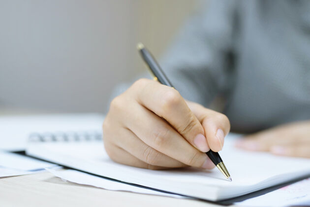 女性年轻女子手里拿着打开的笔记本页 用蓝色铅笔放在带书签的木质桌子上笔记本写作文件