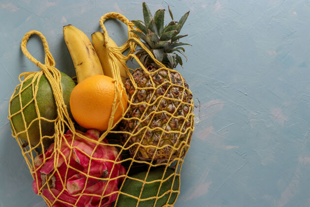 网零浪费的概念 网状纺织袋与新鲜的热带水果：芒果 菠萝 龙 猕猴桃 香蕉和西番莲果浅蓝色表面 横向格式香蕉有机健康
