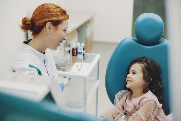 孩子一位年轻的口腔医生和他在儿科口腔科的小病人交谈的侧视图牙痛卷发牙齿