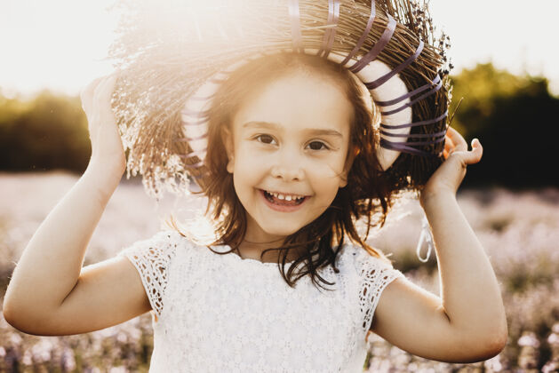 生态照片中 一个可爱的小女孩看着相机 一边笑着 一边拿着头上的花冠 在落日的余晖中 在生物花的领域里微笑人多彩