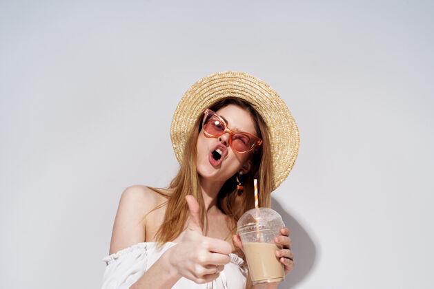 饮料一个戴着粉红色眼镜 戴着帽子的开朗漂亮的女人在一个玻璃杯里喝着一杯奢华的饮料女士成人食物