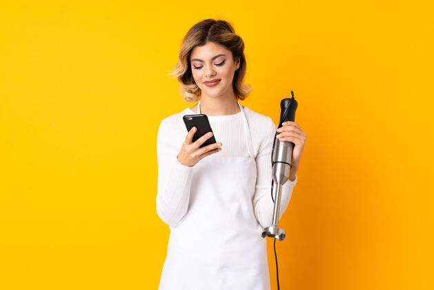 通话女孩用手提搅拌机隔离在黄色的手机上发短信智能讲话青少年