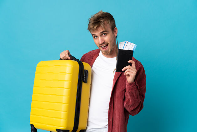 游客年轻英俊的金发男人带着手提箱和护照在蓝色的度假中与世隔绝设备男人旅行
