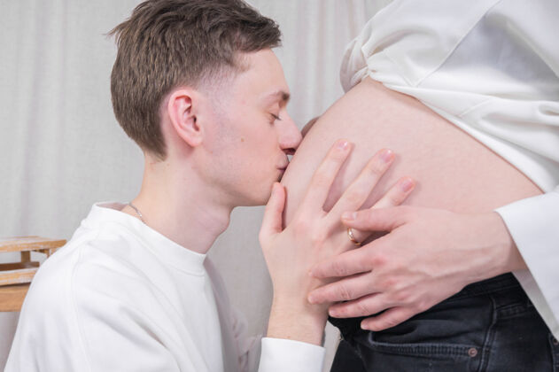 室内年轻的爸爸亲吻怀孕的肚子男人怀孕亲吻