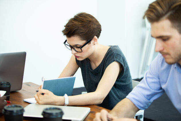 表情新解决方案戴自信一位穿着时髦休闲服的年轻女士坐在办公室的工作场所 一边用笔记本电脑工作互联网休闲商务