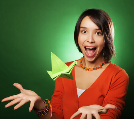年轻一个年轻的表情女人 在绿色的墙壁上带着纸鸟肖像牙齿微笑
