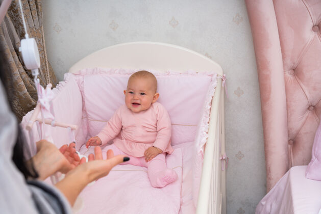 人妈妈的视角和微笑的宝宝在卧室里用粉色婴儿床的场景小孩子封闭